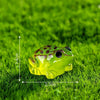 A bright green glow-in-the-dark resin frog ornament resting on vibrant green grass.