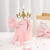 Un gâteau rose décoré d'un grand nœud rose et d'un candélabre doré sur un support blanc.