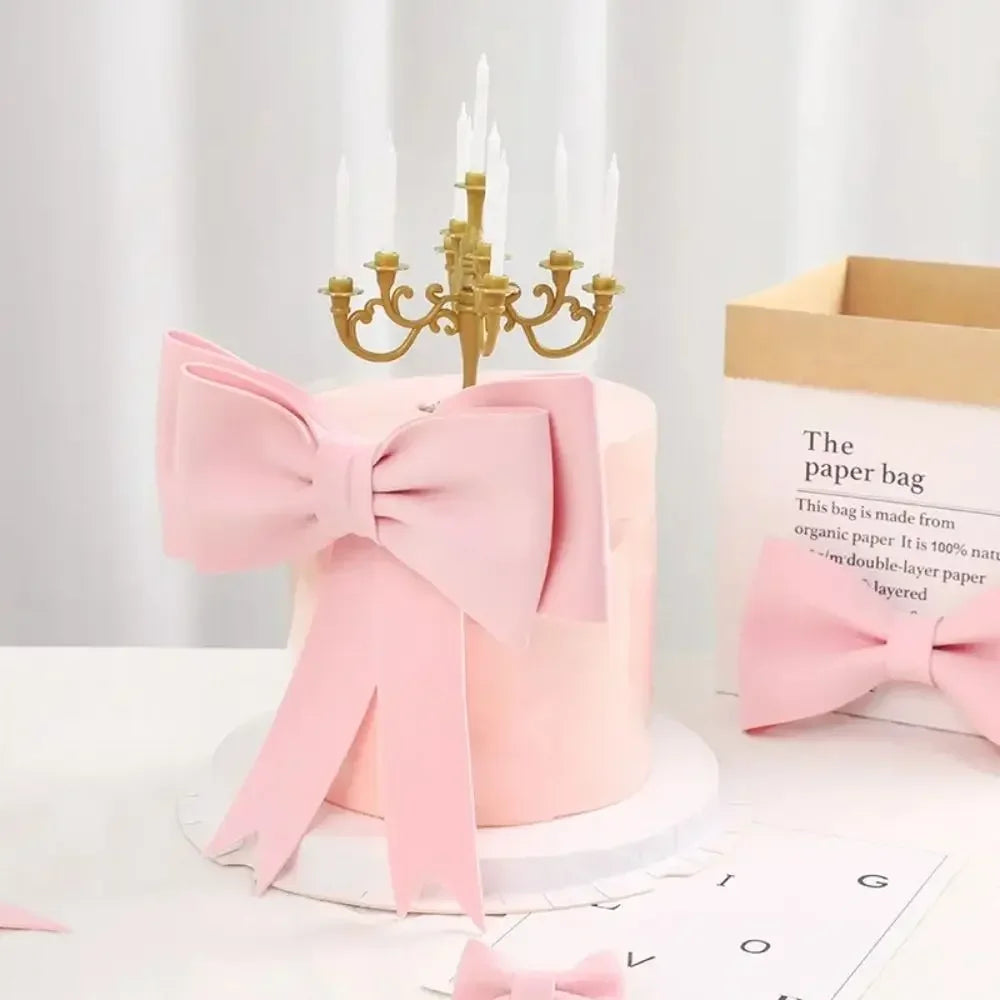 Un gâteau rose décoré d'un grand nœud rose et d'un candélabre doré sur un support blanc.