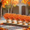 An arrangement of bright orange and red artificial autumn flowers in pots displayed on a stone ledge.