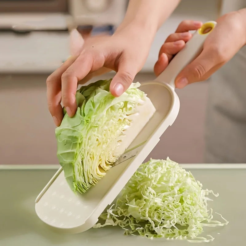 A hand is using a manual cabbage shredder to process a head of green cabbage into shreds.