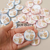 A hand holds a collection of pink and blue cartoon bear team pin badges for gender reveal and baby shower parties