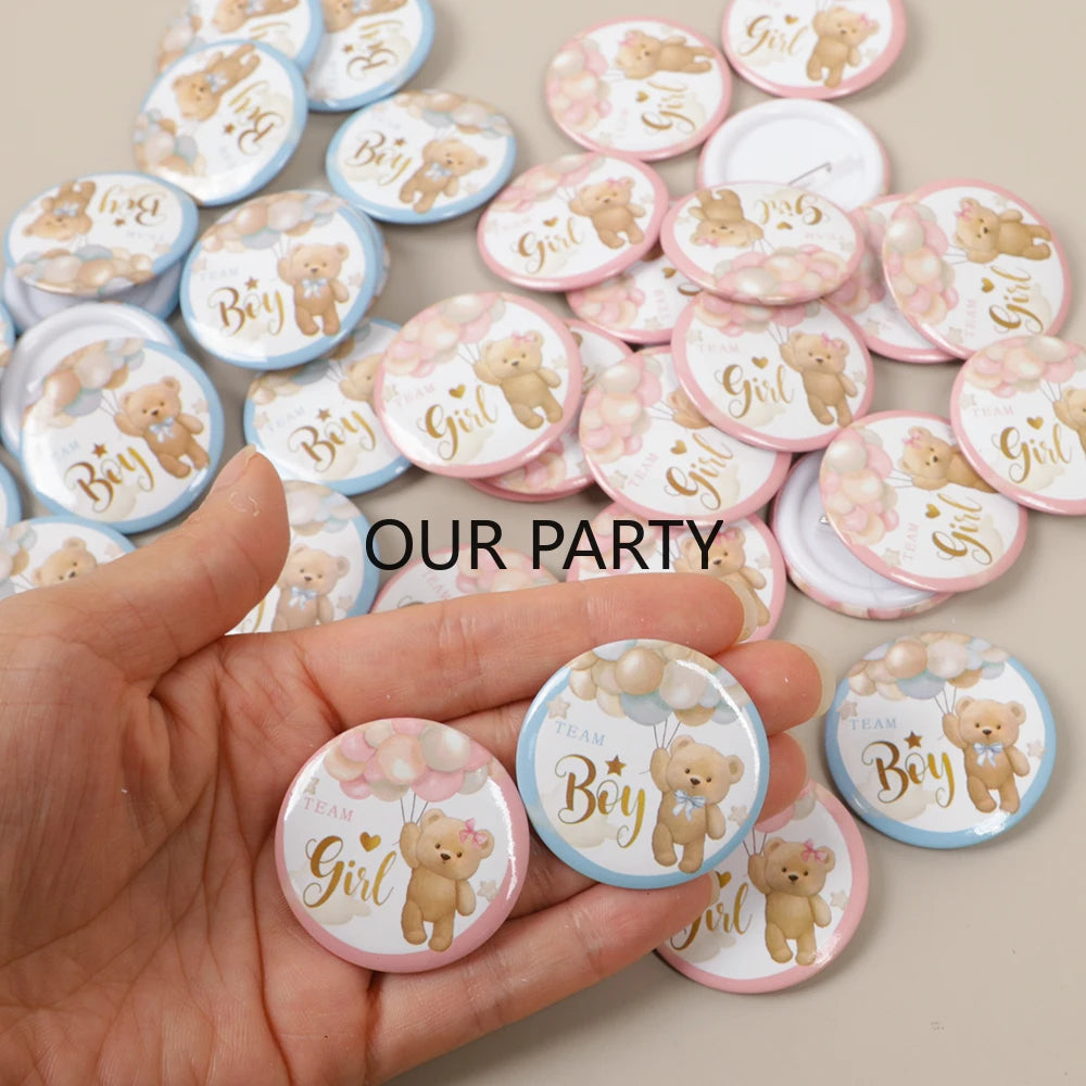 A hand holds a collection of pink and blue cartoon bear team pin badges for gender reveal and baby shower parties