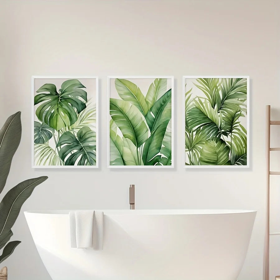 A set of three watercolor leaf art prints featuring lush green tropical foliage displayed on a white wall above a bathtub.