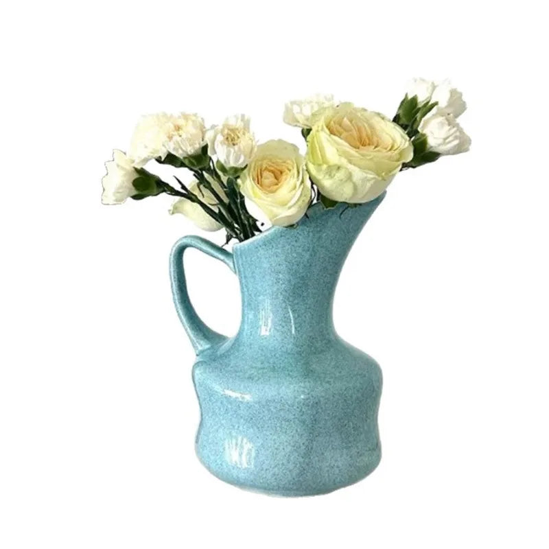 A light blue ceramic vase filled with white roses and greenery.