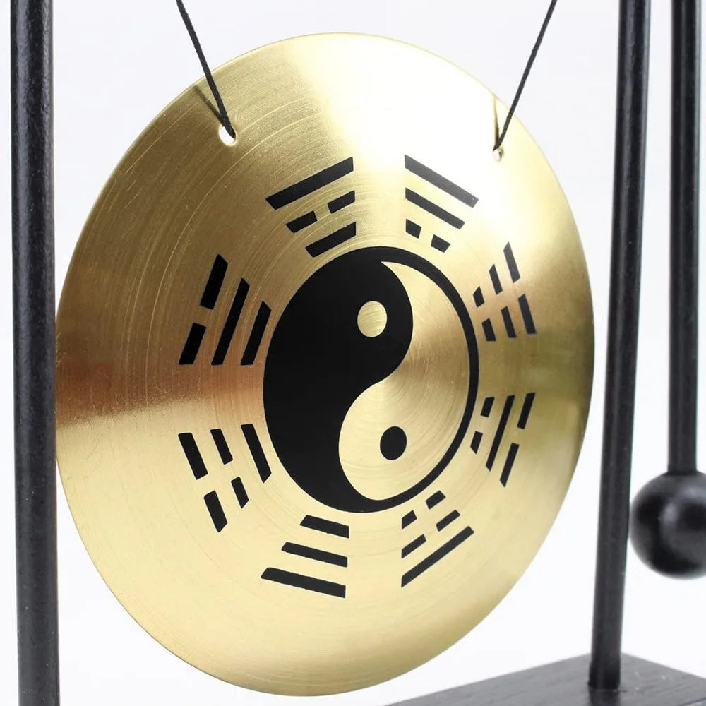 A round brass desktop gong featuring a black yin-yang symbol and radiating lines, suspended by thin black cords.
