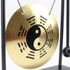 A round brass desktop gong featuring a black yin-yang symbol and radiating lines, suspended by thin black cords.