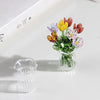 A small bouquet of colorful glass flowers in a clear vase on a white surface.