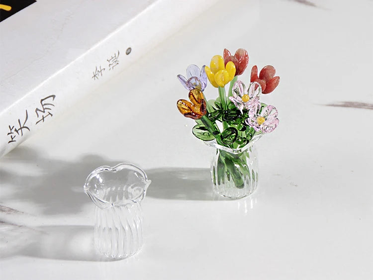 A small bouquet of colorful glass flowers in a clear vase on a white surface.