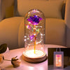 An LED galaxy rose artificial flower displayed inside a glass dome on a wooden base.