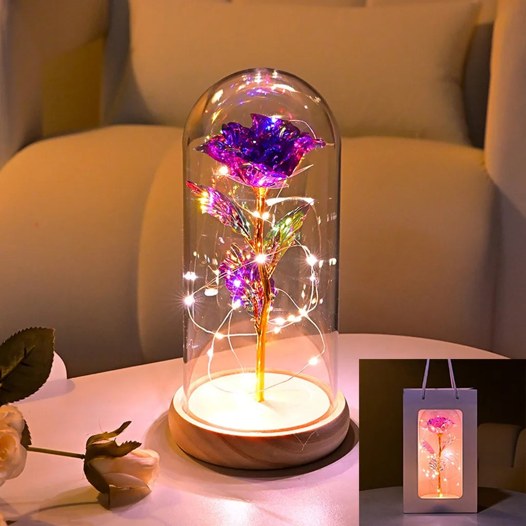 An LED galaxy rose artificial flower displayed inside a glass dome on a wooden base.