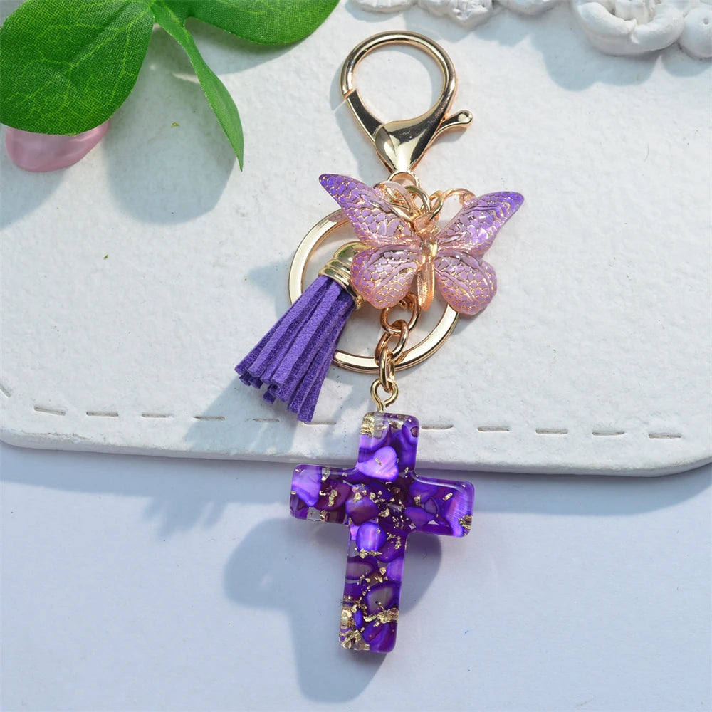 A gold-toned keychain featuring a purple resin cross and a pink butterfly charm