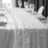 White table draped with sheer white gauze featuring a beaded trim and pearl embellishments.