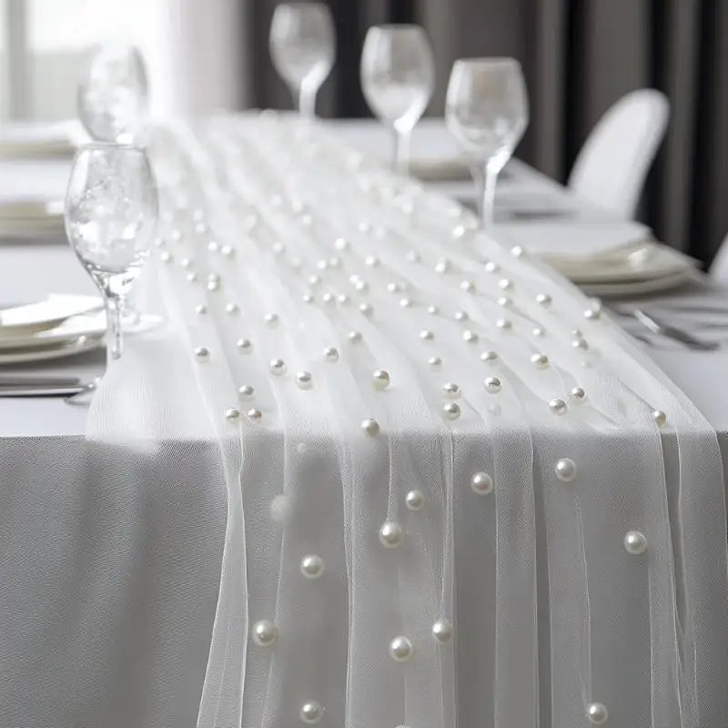 White table draped with sheer white gauze featuring a beaded trim and pearl embellishments.