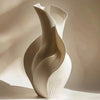 A beige ceramic vase with an abstract, flowing grass motif, photographed in soft natural light.