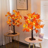 An orange maple tree decoration with lights sits on a gold-framed table.