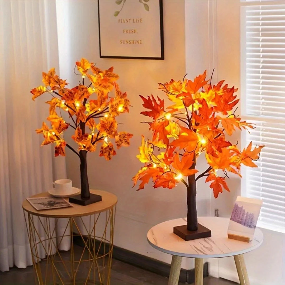 An orange maple tree decoration with lights sits on a gold-framed table.