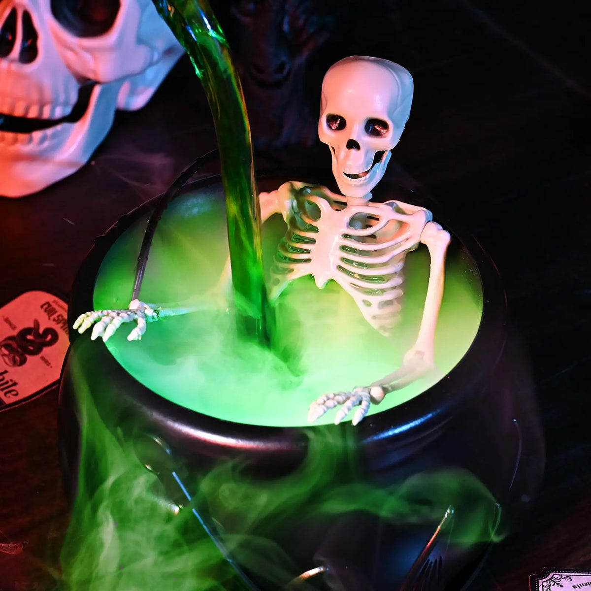 A black cauldron filled with glowing green liquid and a white skull skeleton figure emerging from the mist.
