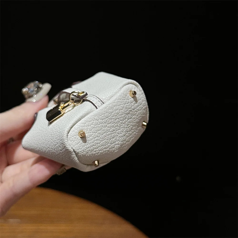 A hand holds a small, beige leather handbag with a gold wrist strap against a dark background.