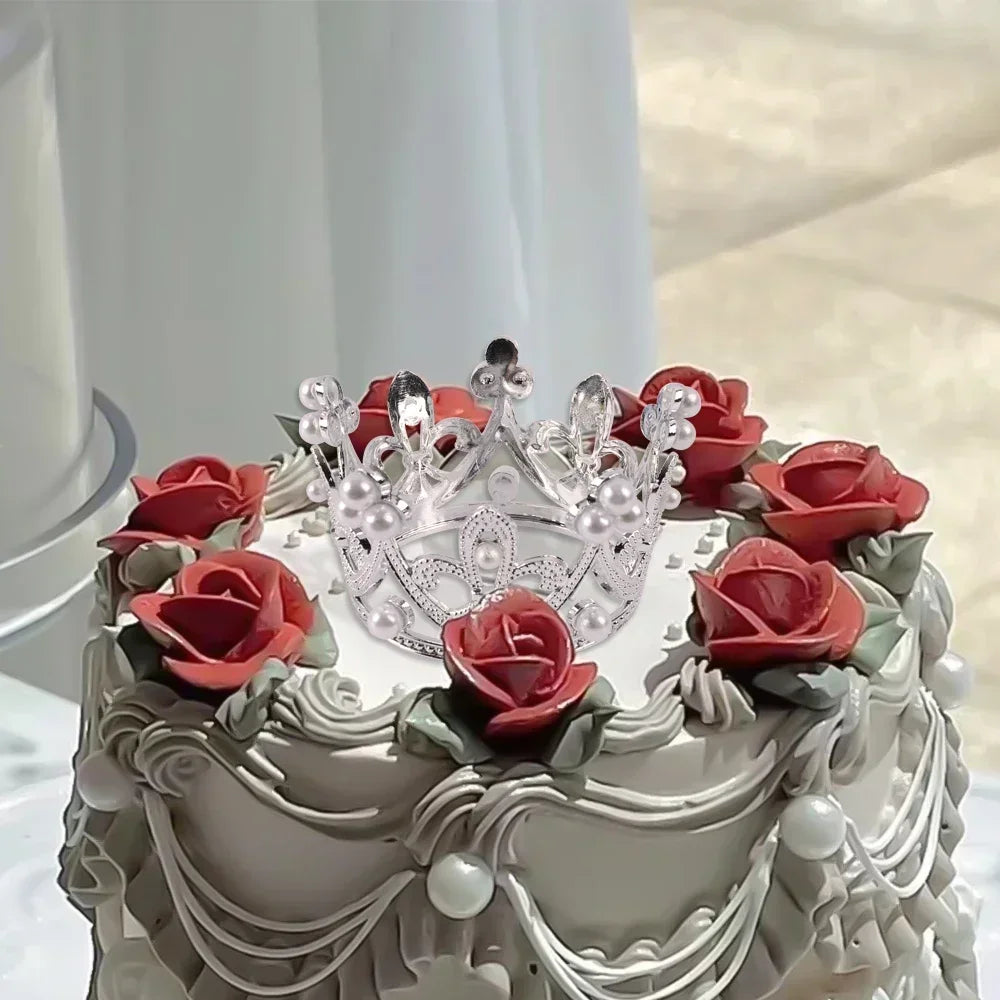 A white cake decorated with red roses and silver crown toppers.