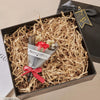 A gift box filled with crinkle cut paper shred filler containing a small arrangement of red roses and a card