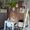 A white table is set against a textured brick wall decorated with clocks and greenery, next to a wooden ladder.