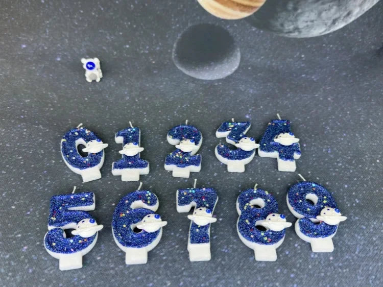 A set of twelve blue planet design birthday candles for ages 1 through 9 arranged on a dark gray surface.