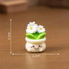 A small white resin charm shaped like a potted plant with green leaves and a smiling face.