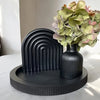 A black striped silicone mold for vases and trays is displayed on a round black wooden base with a bouquet of green and pink 