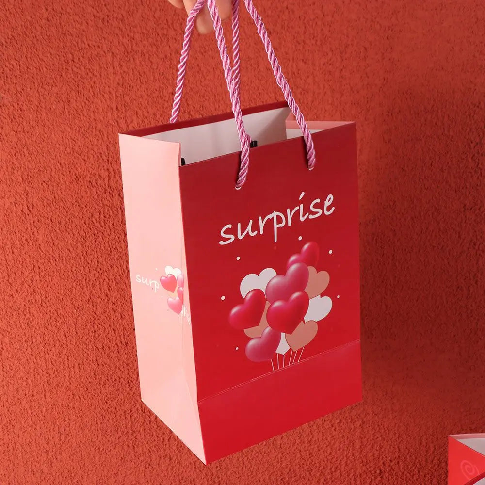 A red gift box with pink accents and a surprise tag is held by a hand against an orange background.