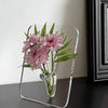 A clear acrylic frame vase holding pink dahlia flowers on a dark surface.