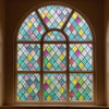 A close-up of a arched stained glass window featuring multicolored diamond patterns.