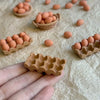 A hand holds a small, light brown, waffle-patterned mold filled with pinkish-orange spherical items.