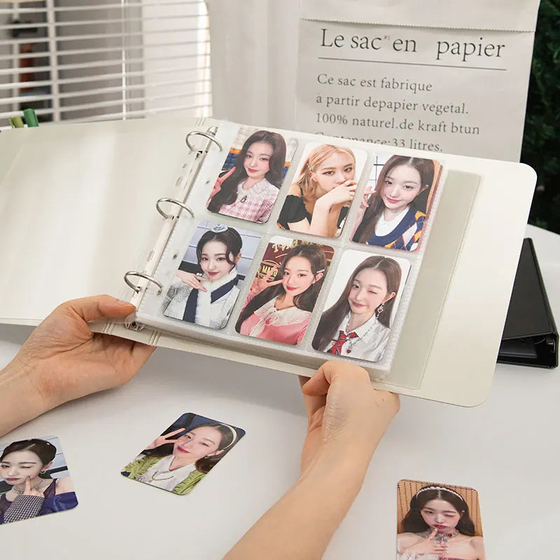 A hand is holding an open K-Pop photo card binder displaying several glossy photos of female idols.