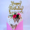 A white cake decorated with gold butterfly designs and a gold script topper that reads Happy Birthday