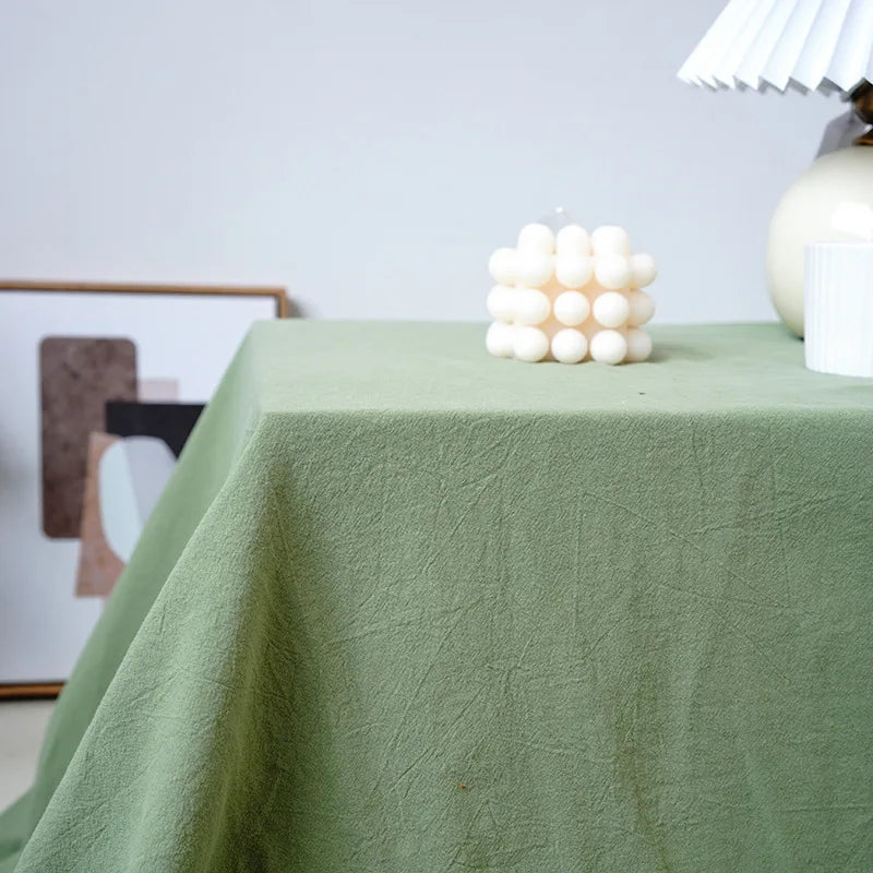 A light green cotton rectangle tablecloth is draped on a table, featuring a cluster of white decorative balls.
