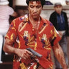 Un homme en chemise rouge à motifs tient une arme de poing, probablement du film Scarface, dans une scène dramatique.
