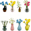A collection of seven mini ceramic plant vases holding colorful flowers like blue, yellow, and pink blooms.