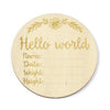 A round natural wood baby milestone disc with the text Hello world and lines for name date weight and height.