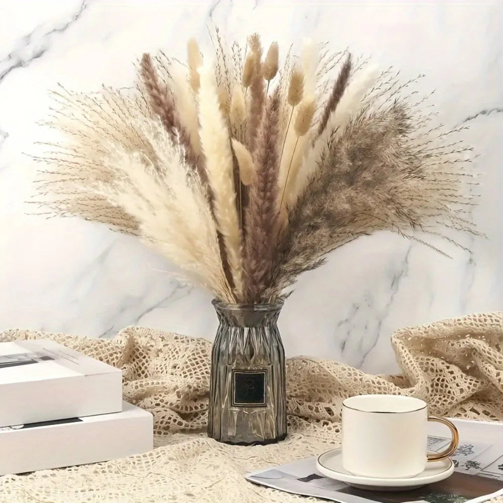 A dried flower bouquet of pampas grass in a silver vase resting on a textured fabric surface.