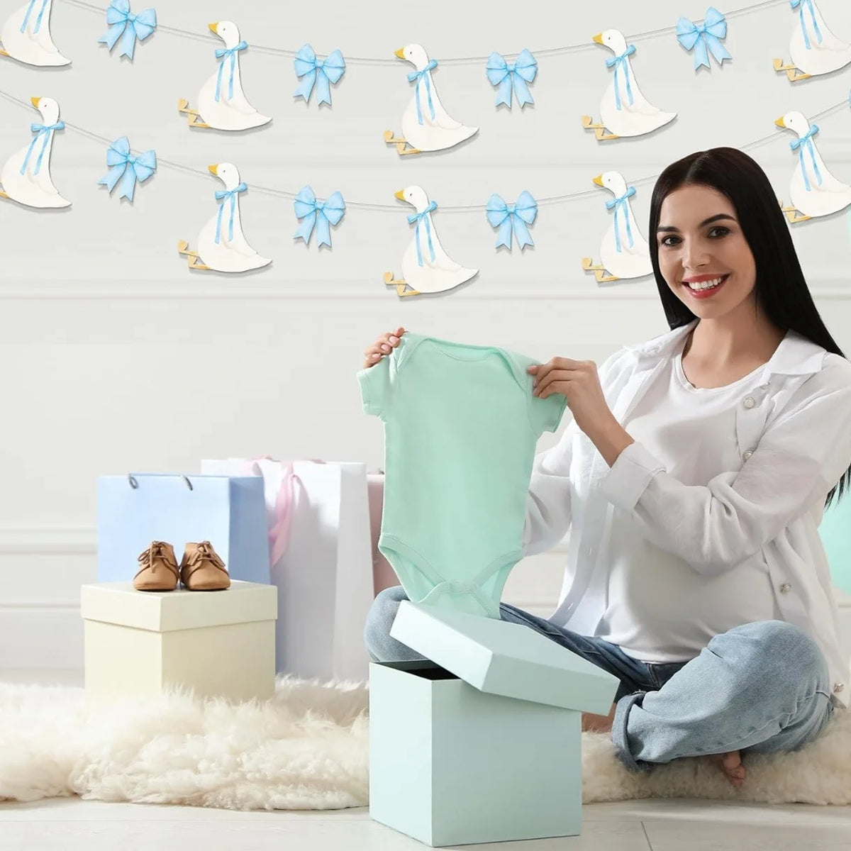 A woman holds a light green baby outfit in front of a banner featuring white goose shapes with blue bow knots.