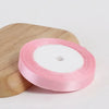 Pink silk satin ribbon rolled on a light wooden cutting board.