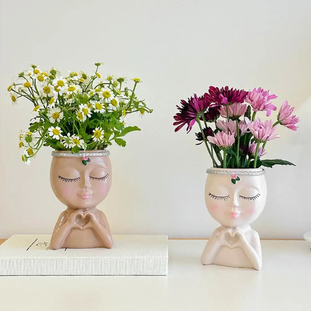 A small artistic resin girl face planter with a drainage hole holds a bouquet of white and pink flowers.