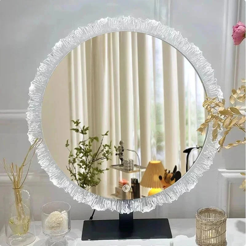 A round, silver-framed vanity mirror with a sunburst design sits on a black stand.