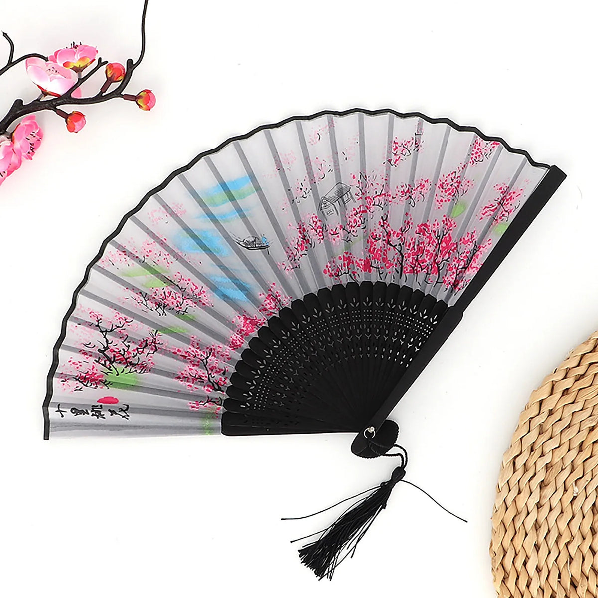 A black folding fan with pink and green fabric patterns, featuring cherry blossoms and birds.