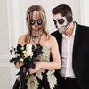 A woman wearing a full face horror costume mask and holding a bouquet of white and black flowers next to a man with a skull m