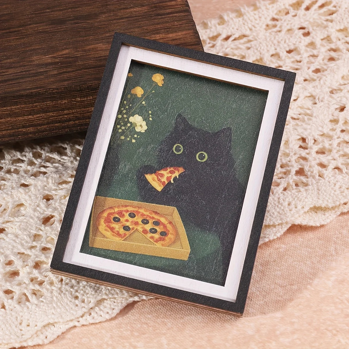 A framed print featuring a black cat and a slice of pizza on a dark green background.