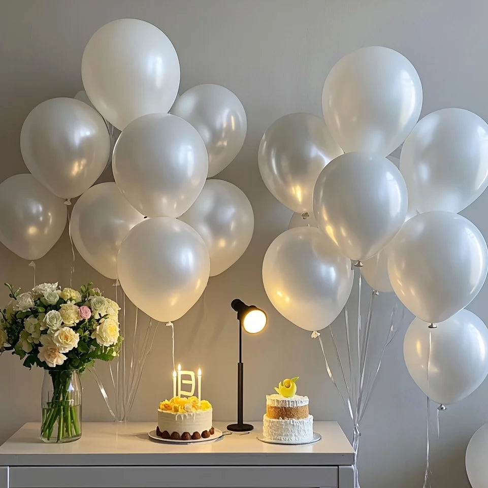 A display of pearl white latex balloons, some clustered and others floating, alongside a cake and a lamp.