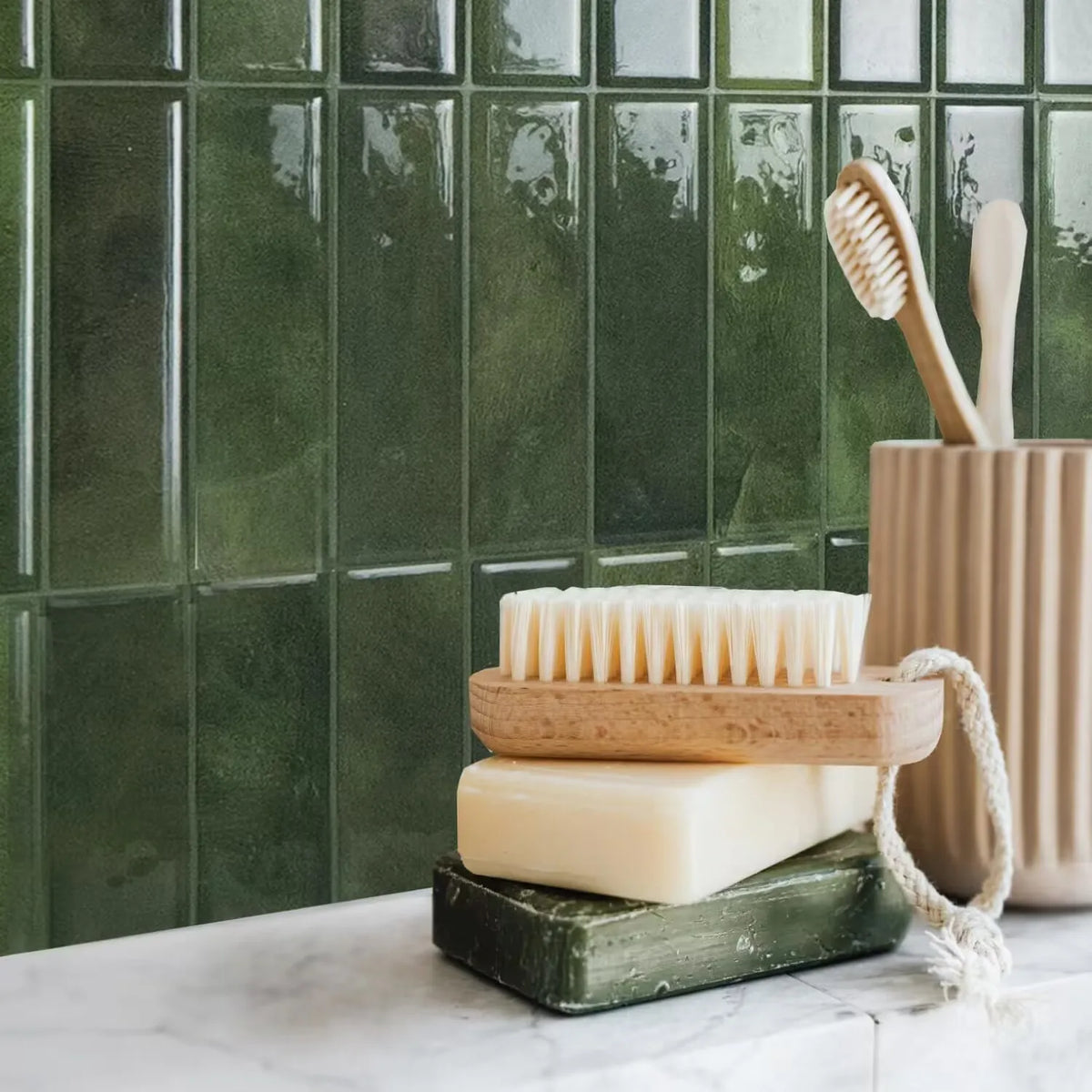 A display of natural soap bars and wooden toothbrushes against a dark green tiled backsplash.