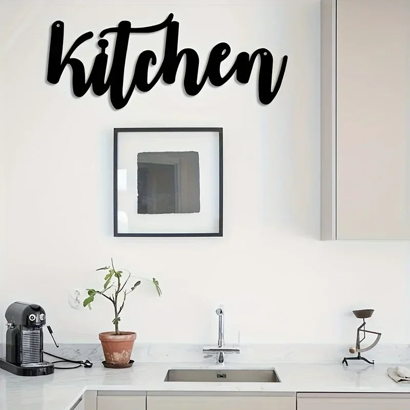 Black script wall art spelling kitchen above a white countertop with a sink and faucet.